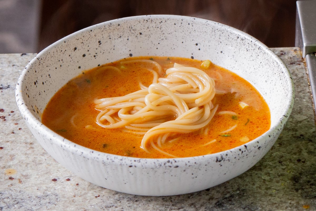 adding ramen noodles to the bowl of spicy peanut butter broth