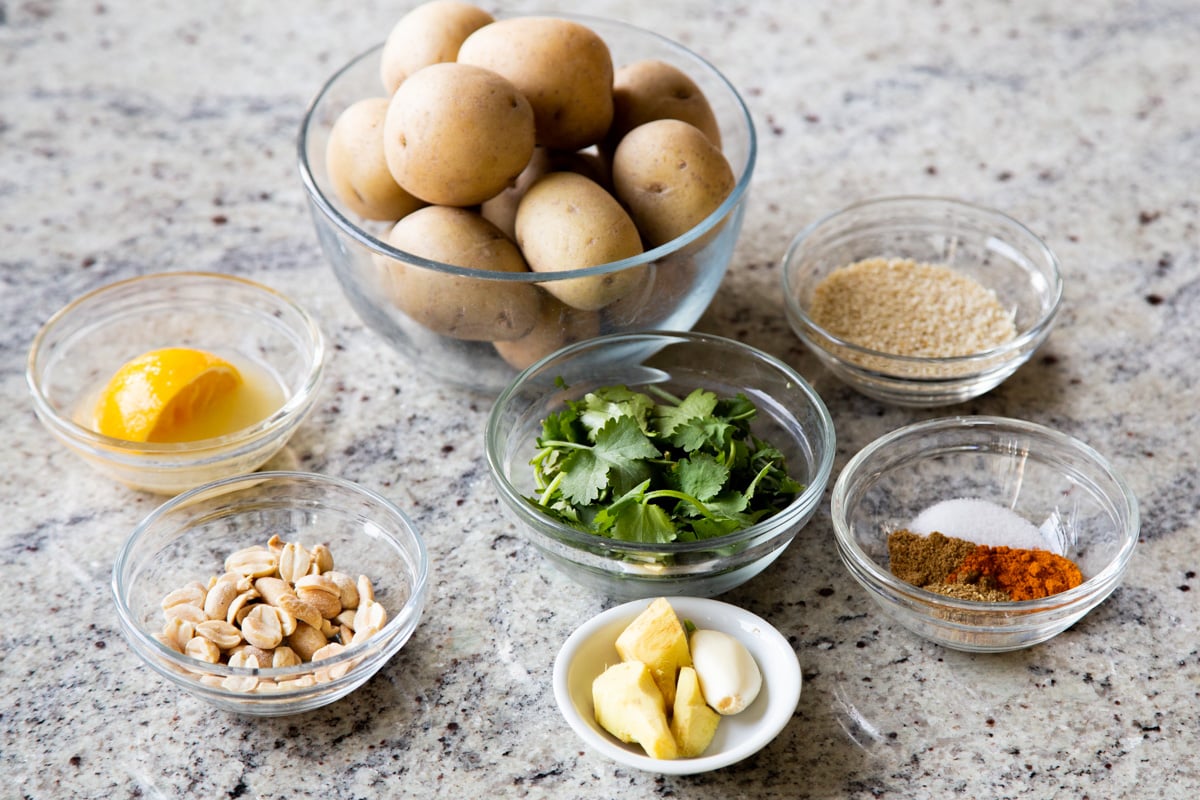 potatoes, peanuts, sesame seeds, and spices in bowls on a kitchen countertop