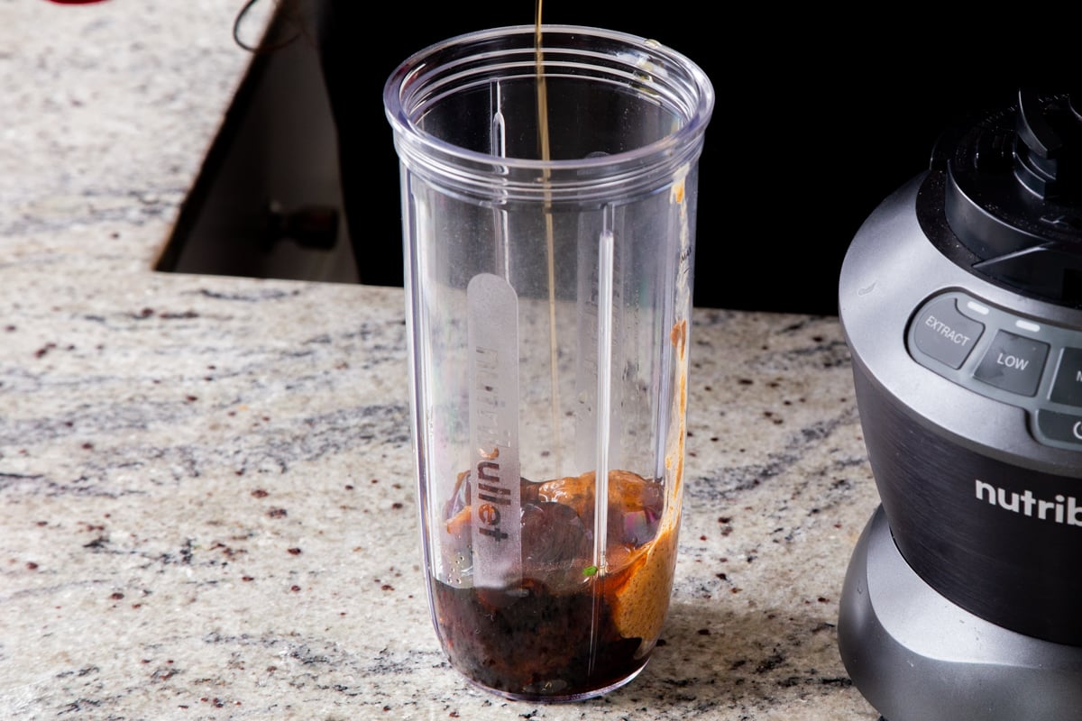 adding maple syrup to the blender with the dates in it