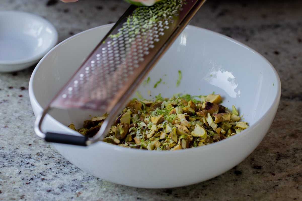 zesting a lime into a bowl of chopped pistachios