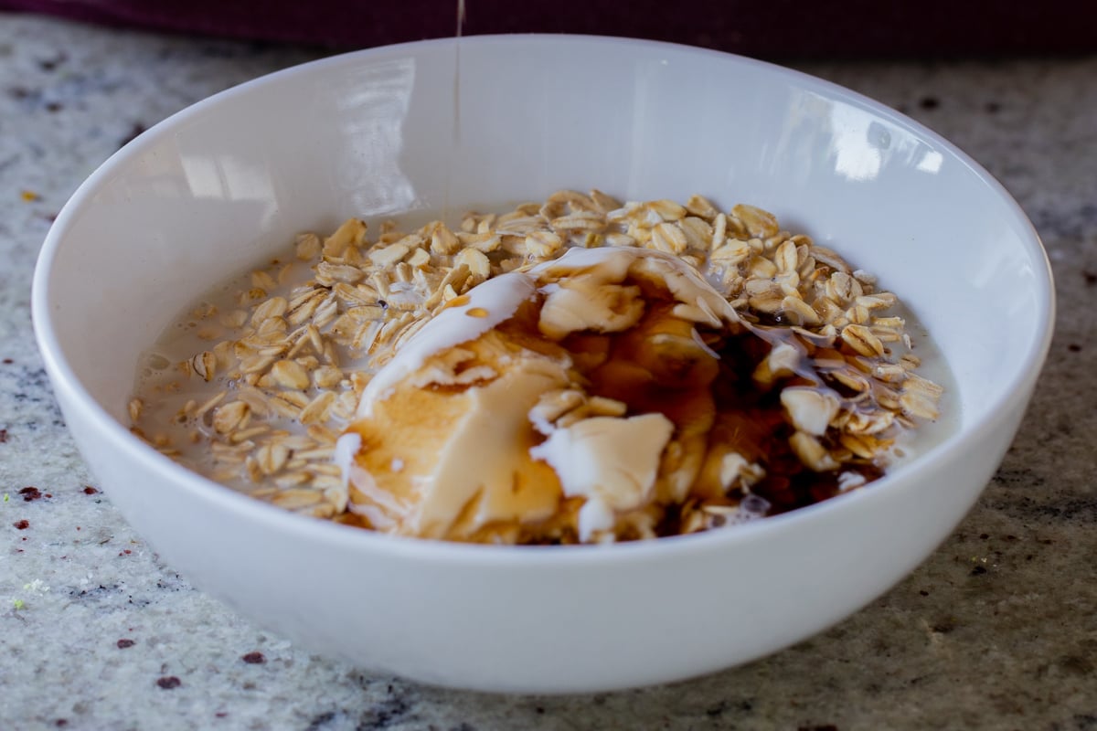 adding maple syrup and non-dairy yogurt to the bowl of oats