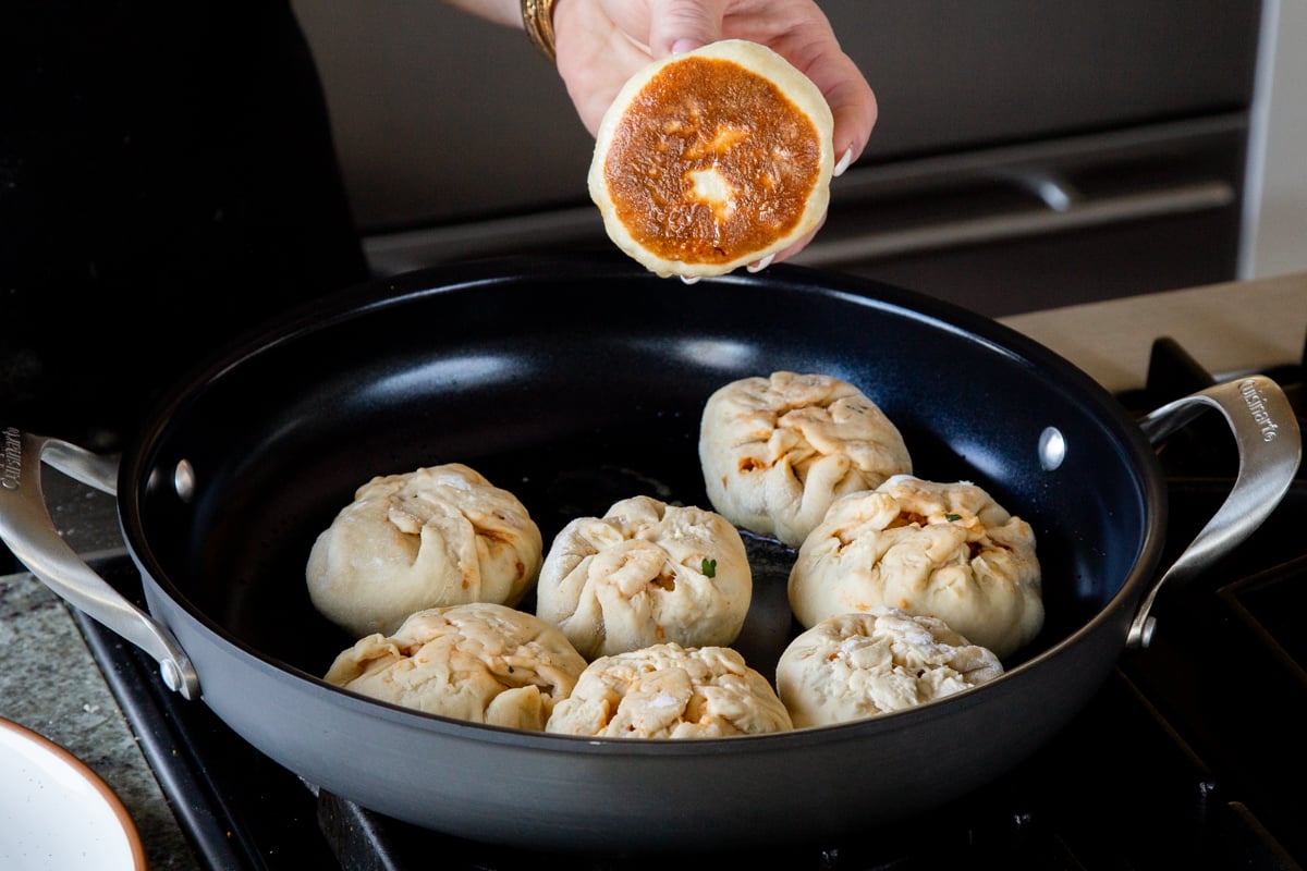 butter chicken bao in the pan, hand holding one up, so you can see the browned bottom