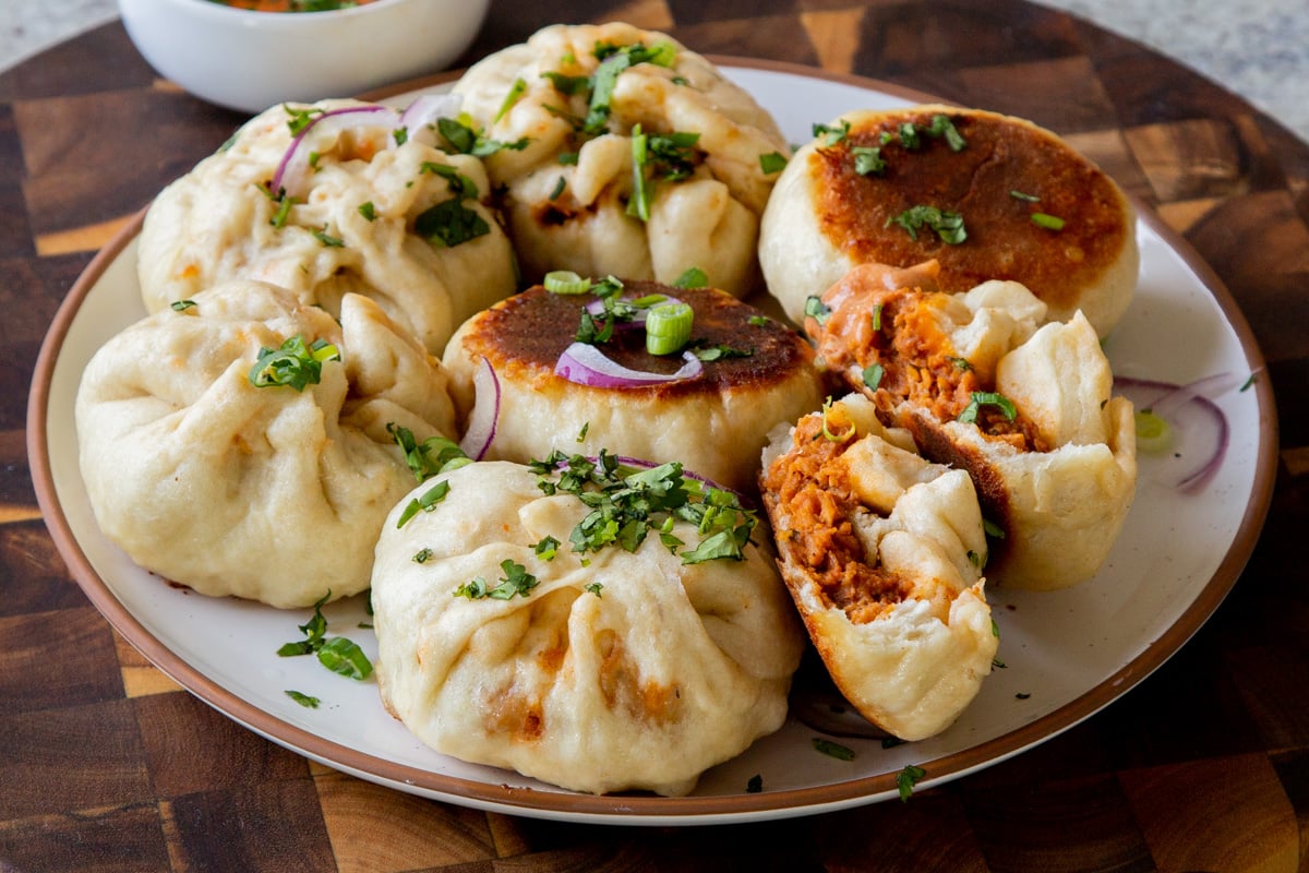 serving plate of butter chicken bao with one flipped so you can see the crispy bottom and one town in half so you can see the filling