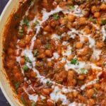 close-up of a panful of harissa chickpeas after cooking with cilantro garnish and coconut cream swirl
