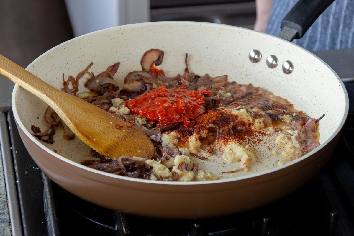 adding harissa and other spices to the frying pan