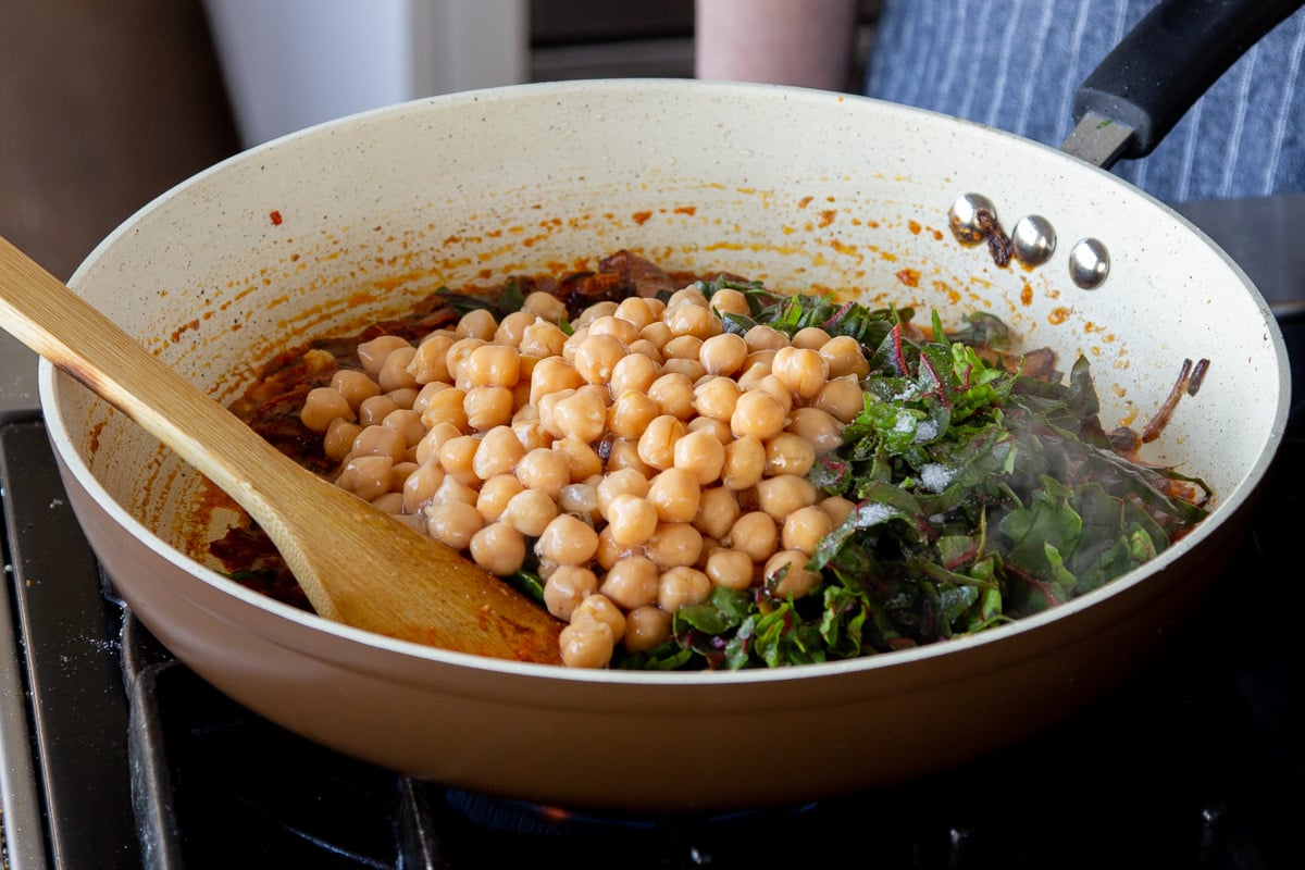 adding Swiss chard and chickpeas to the pan of harissa onions