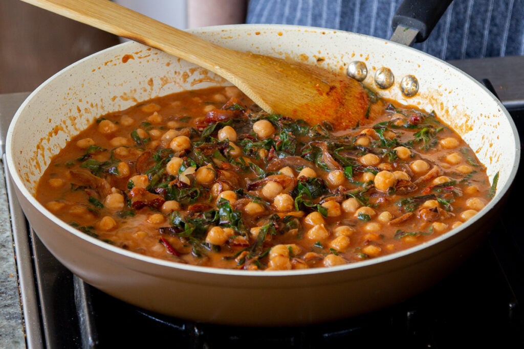 cooking down the greens in the pan of chickpeas