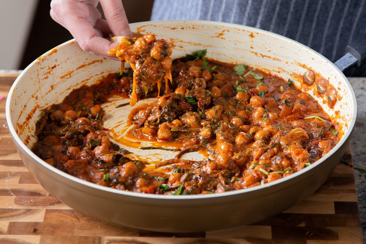 dipping naan into a panful of harissa chickpeas, pieces of caramelized onion hanging off of the edge of the naan