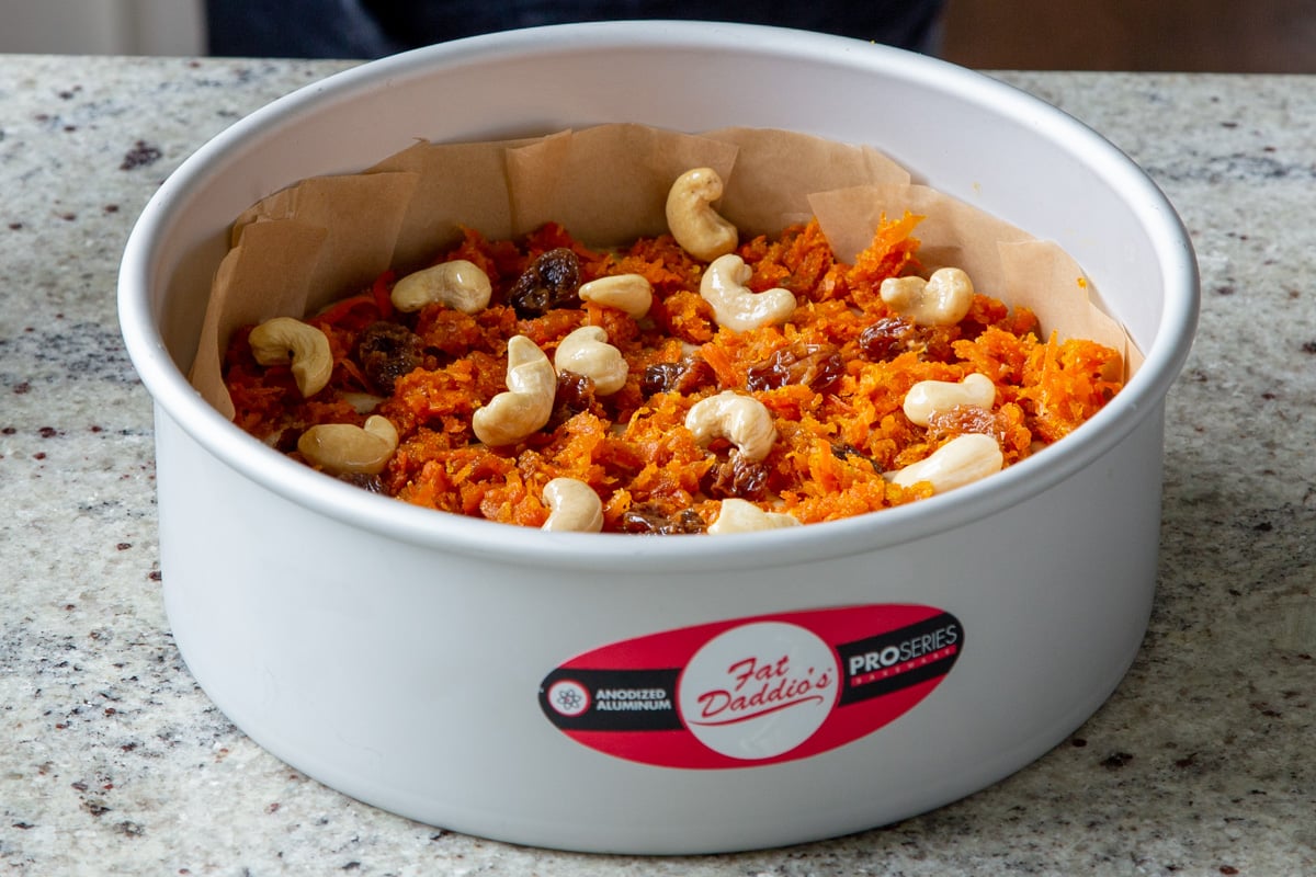 cashews and raisins on top of the carrot mixture in the cake pan