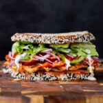 vegan club sandwich with veggies and tofu deli meat on a wooden cutting board