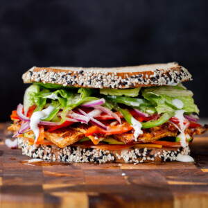 vegan club sandwich with veggies and tofu deli meat on a wooden cutting board