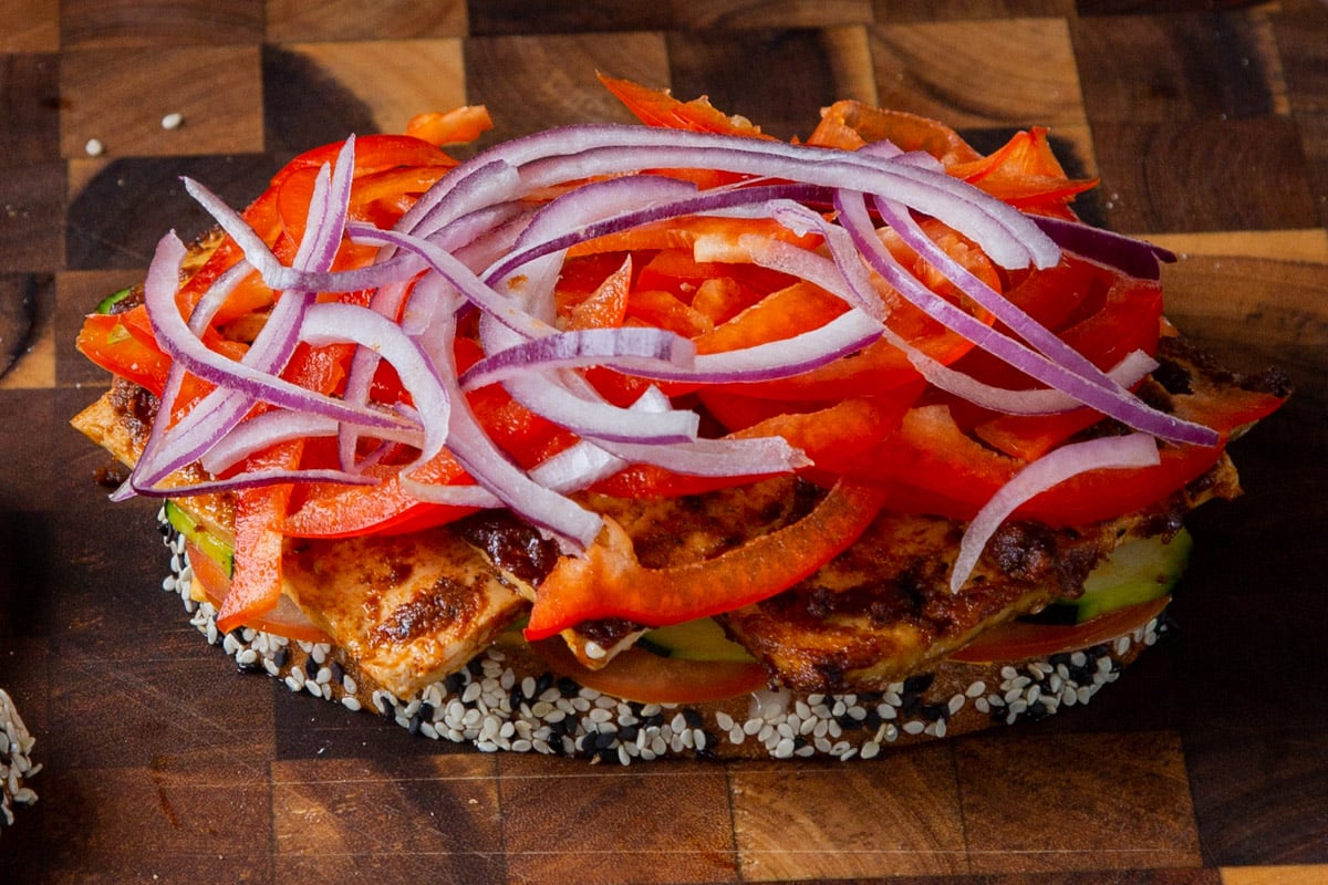 layering onion and red bell pepper slices onto the sandwich