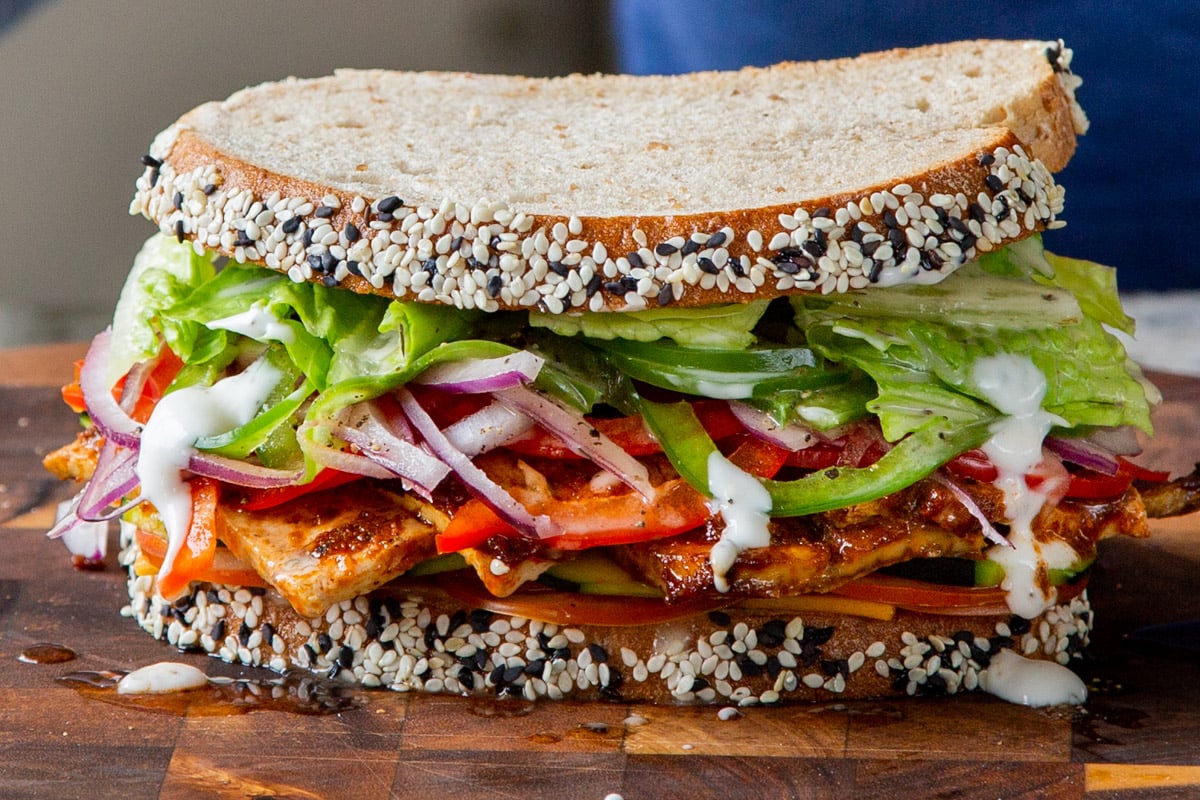 vegan club sandwich with veggies and tofu deli meat on a wooden cutting board