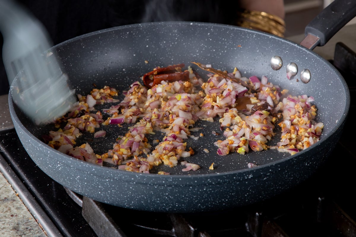 adding onion to the pan of roasted garlic and spices