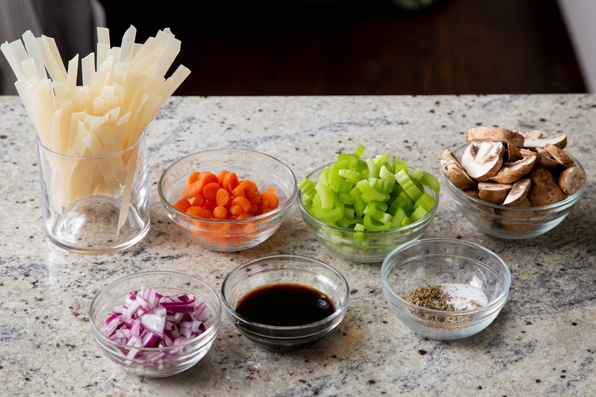 mushrooms, noodles, veggies, and seasonings in bowls on a kitchen counter