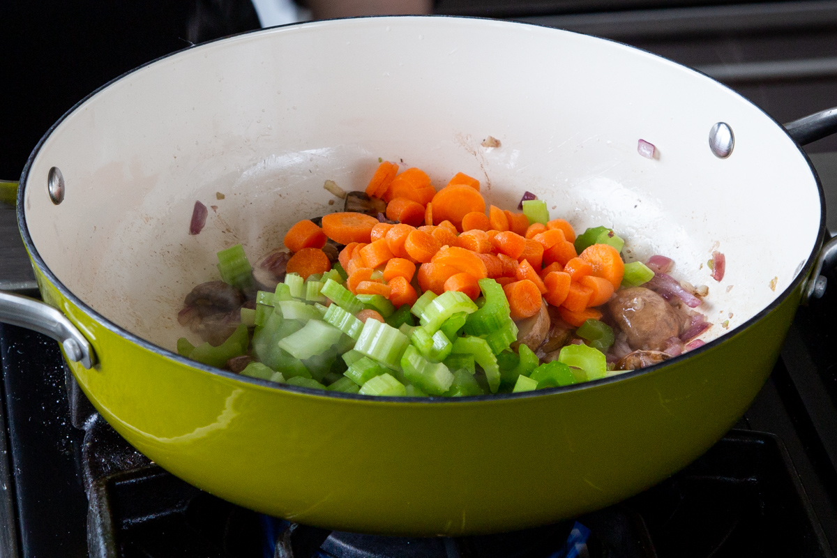 adding veggies to the pan of cooked mushrooms