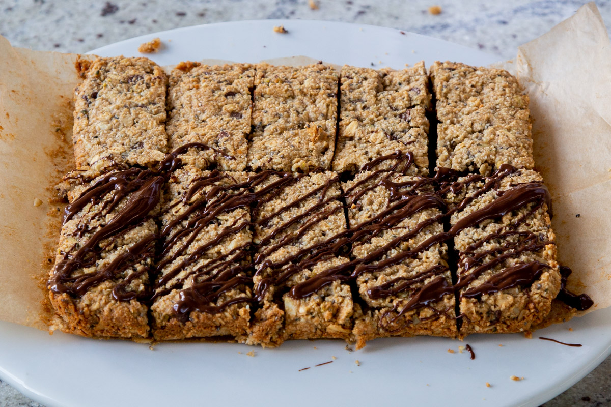 baked granola bars, after slicing, being drizzled with melted chocolate