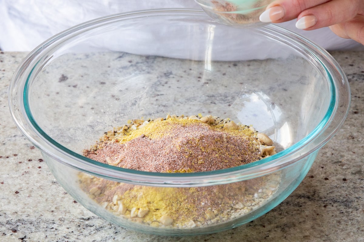 adding spices to the bowl of oats, nuts, and almond flour
