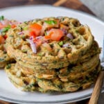 pile of spinach waffles on a plate topped with chopped tomato and cilantro
