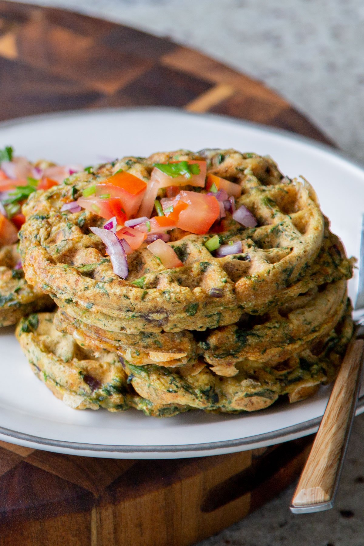 pile of spinach waffles on a plate topped with chopped tomato and cilantro