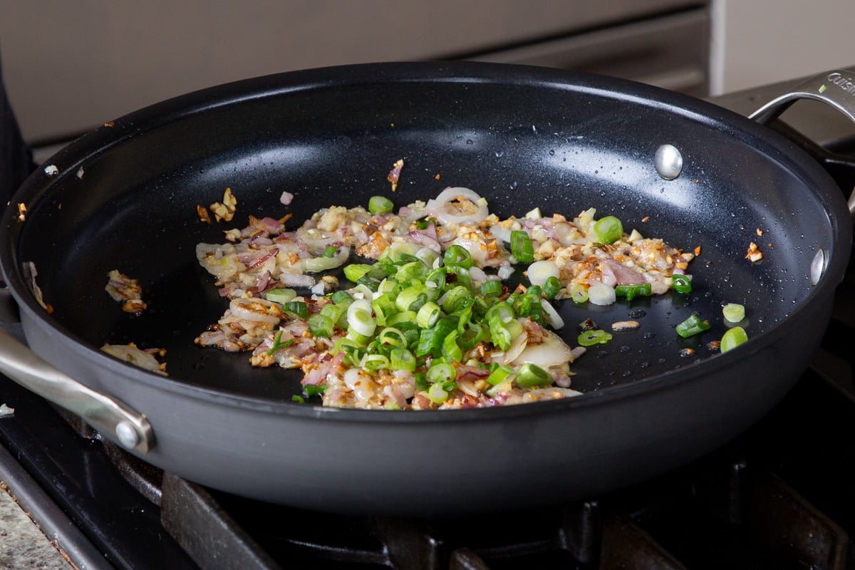 adding green onion to the pan of cooked garlic and onions