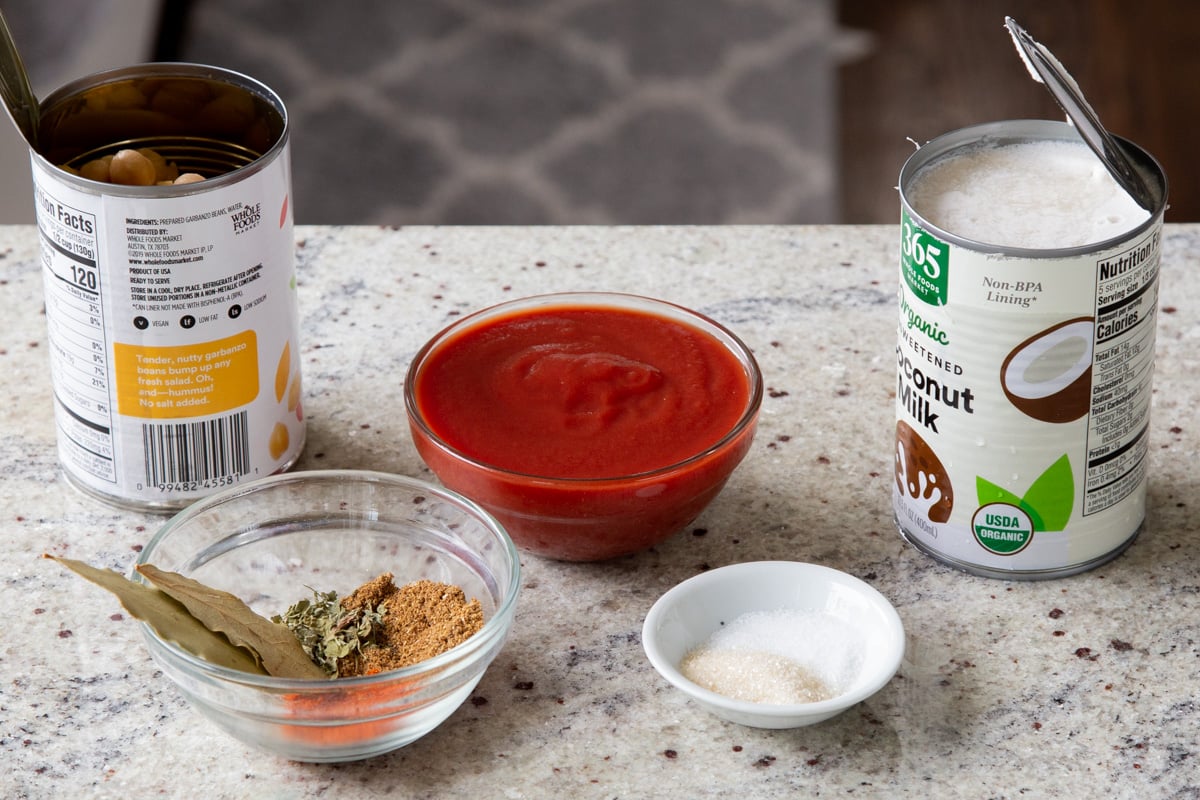 tomato, chickpeas, coconut milk, and spices in cans and bowls on the kitchen counter