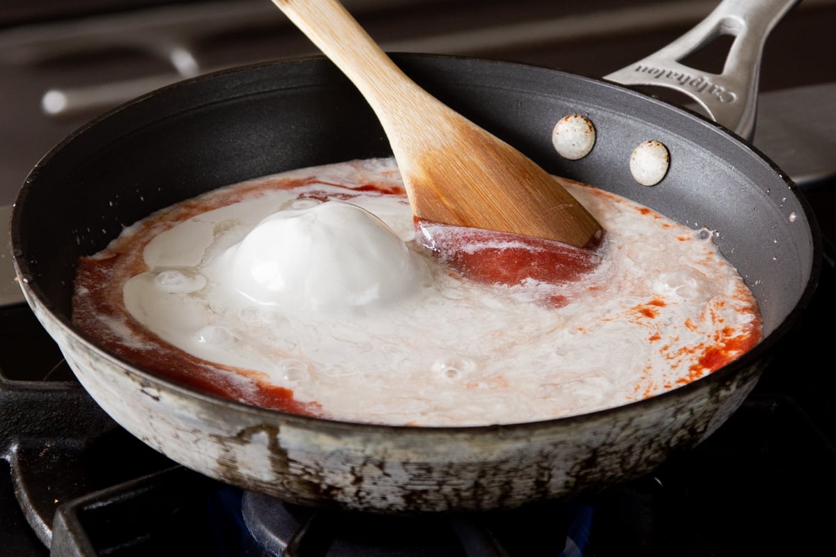 adding coconut milk to the skillet with the tomato puree