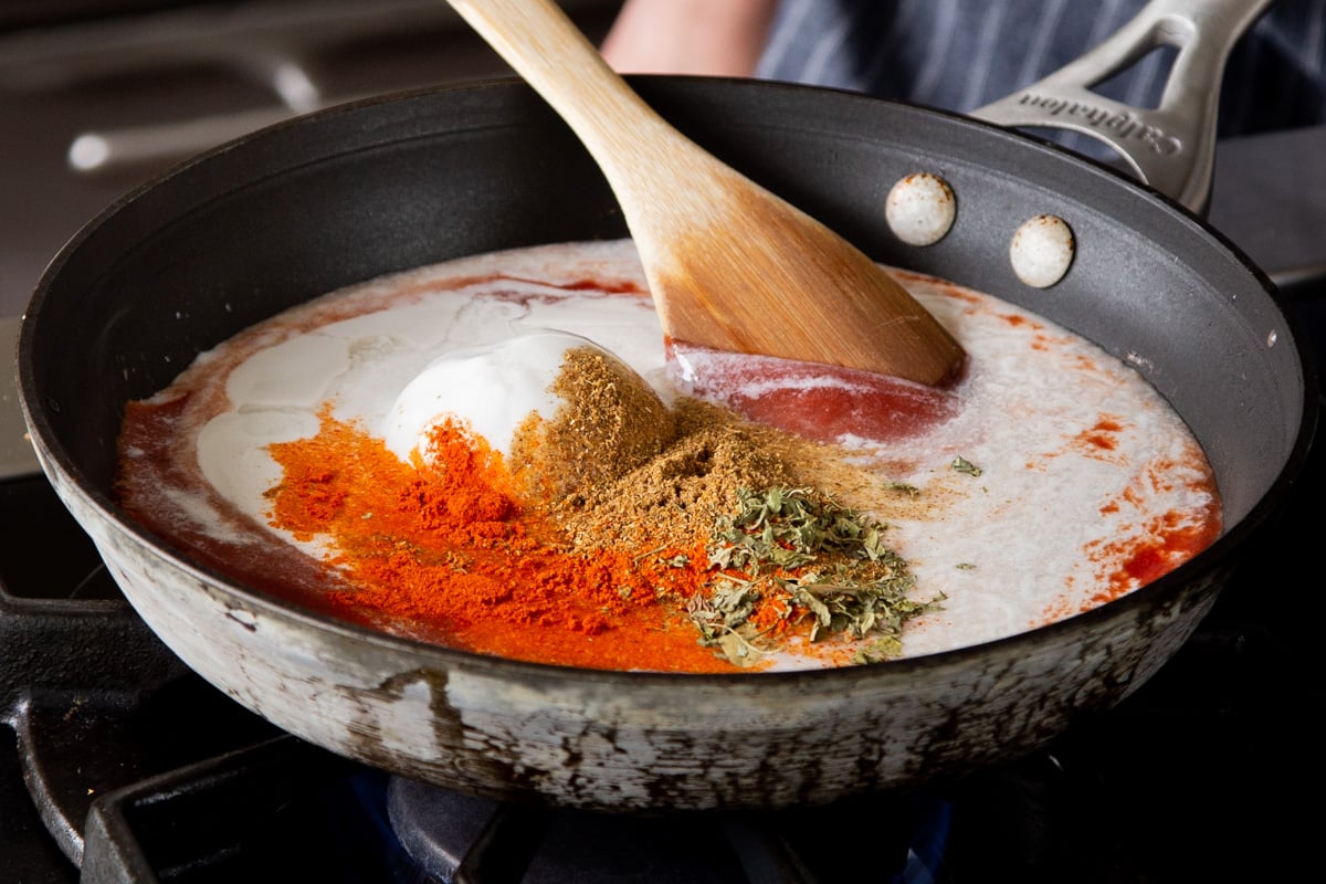 adding salt, sugar, and spices to the skillet with the coconut milk and tomato