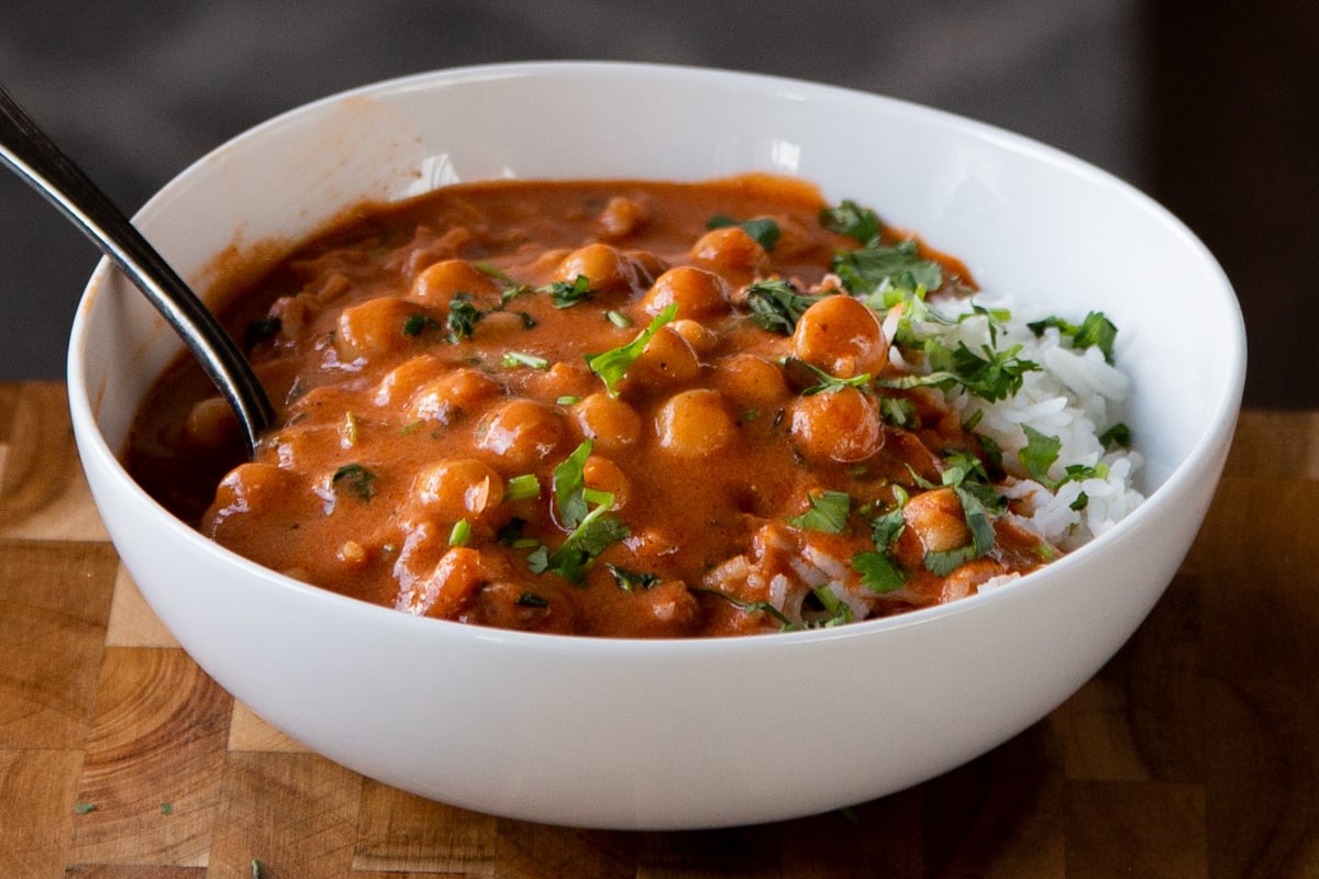 white bowl of butter chickpeas over rice with cilantro on top