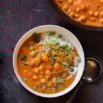 white bowl of butter chickpeas over rice with cilantro on top next to the skillet