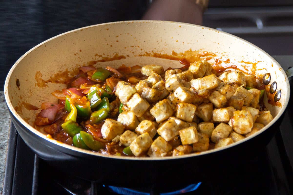 adding tofu to the pan of veggies and honey chili sauce
