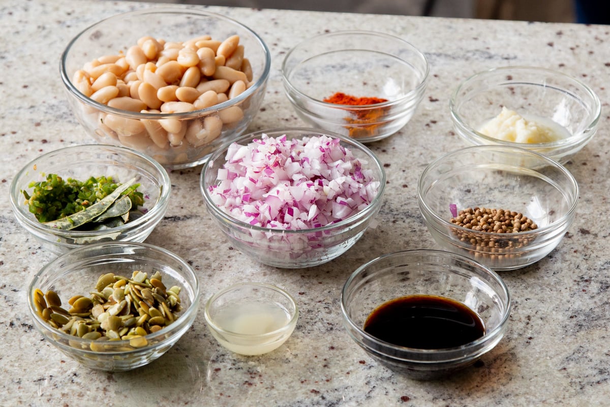 white beans, aromatics, spices, and sauces in bowls on a white table