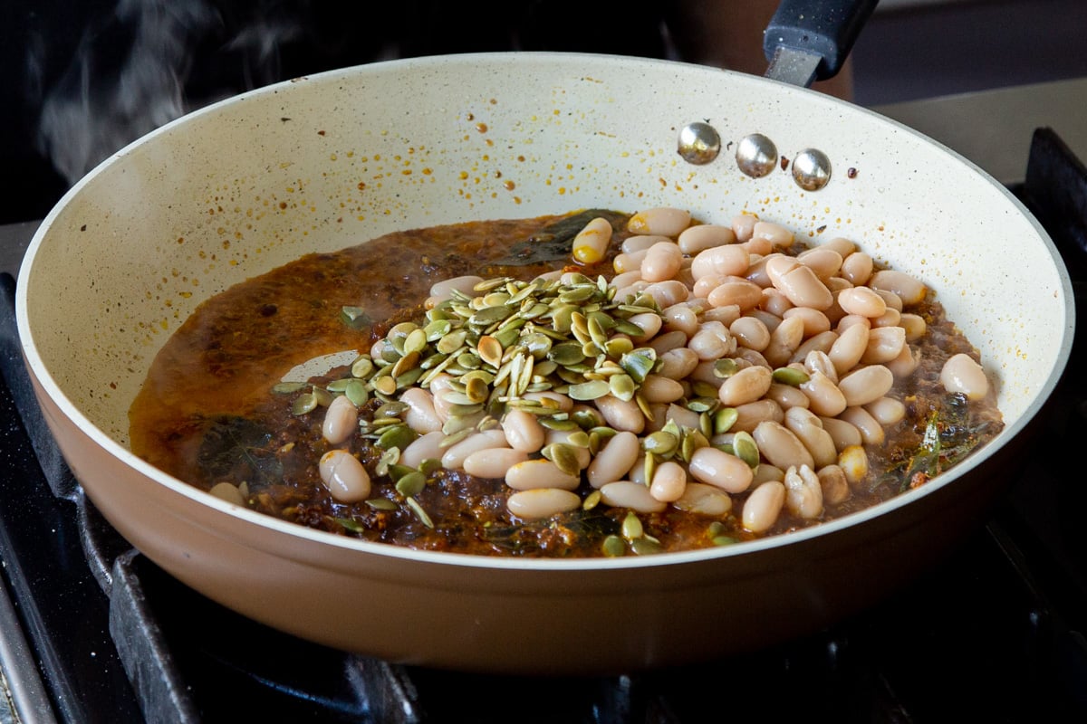 adding white beans and pumpkin seeds to the pan of onion mixture