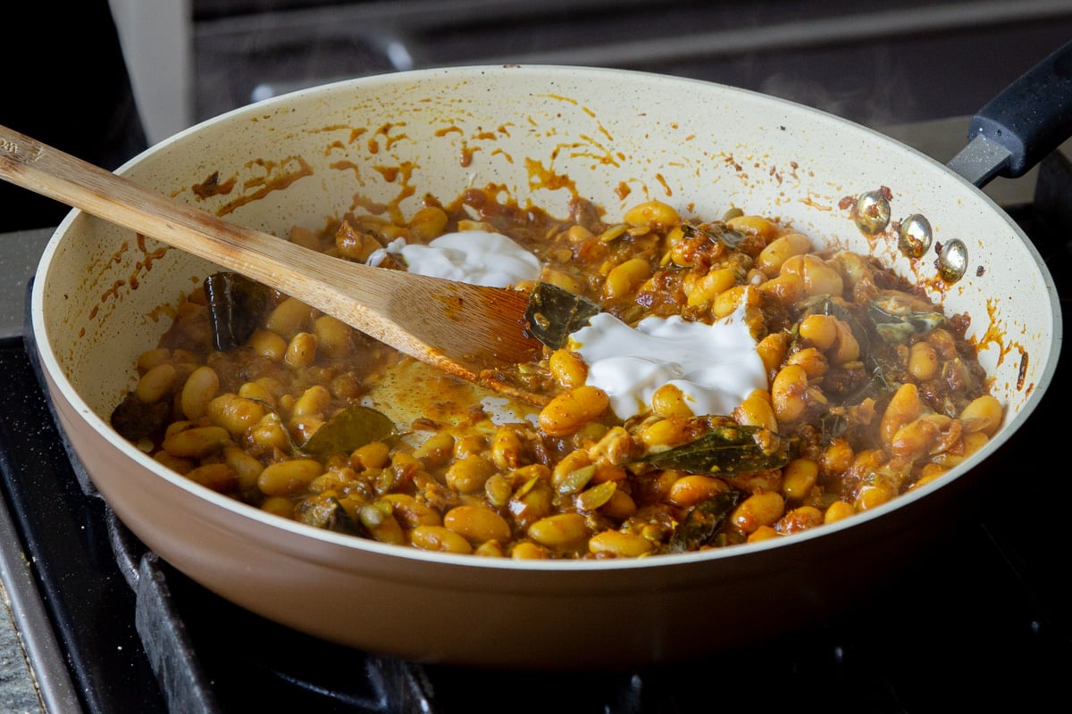 adding yogurt to the pan of white bean stew