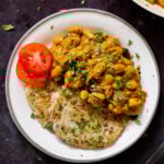 plate of spicy white bean stew with cilantro garnish, naan, and tomato