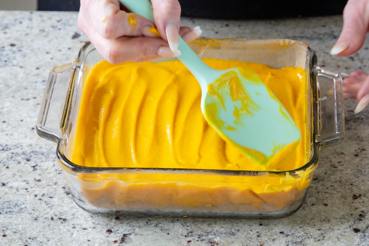 using a spatula to spread the mango custard over the crust