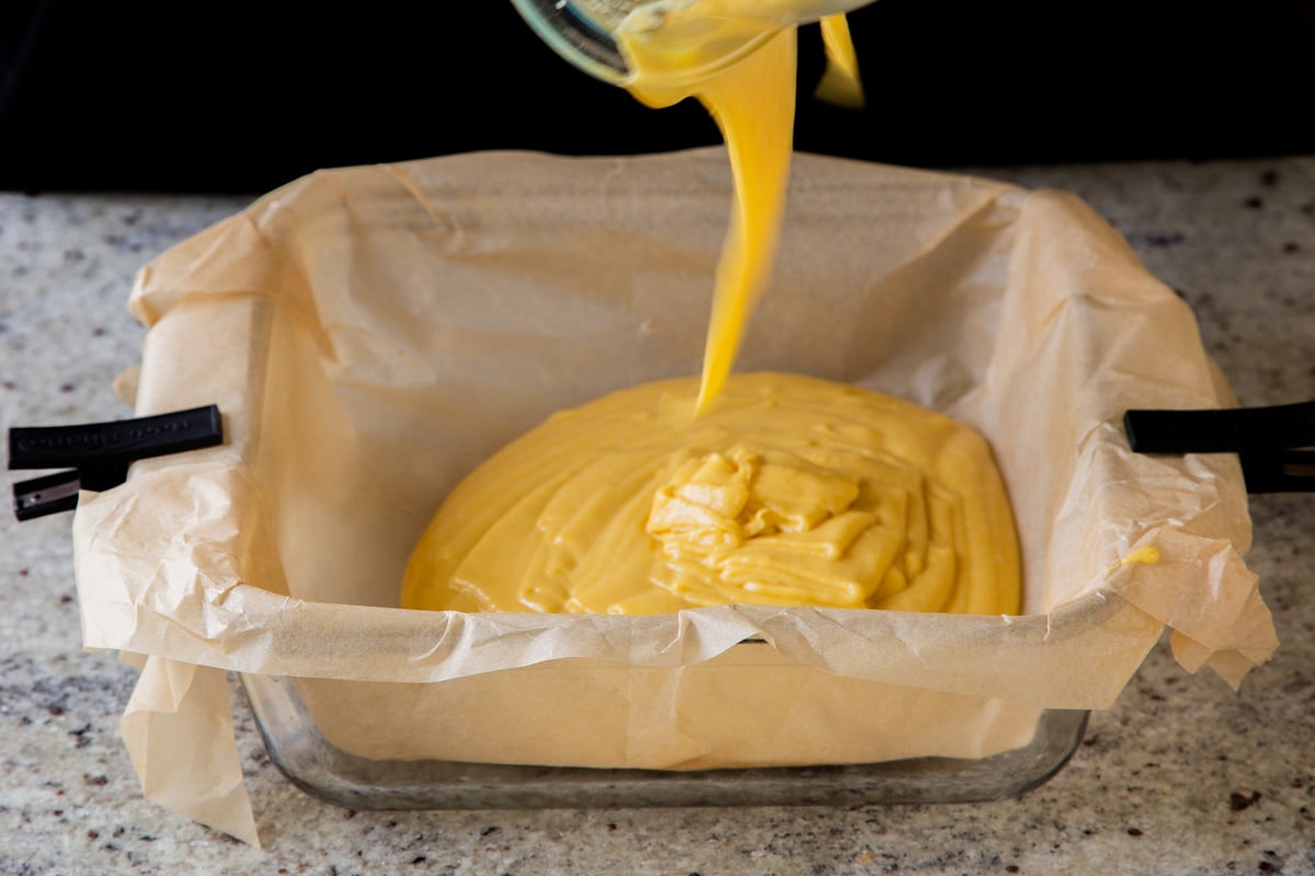 adding mango cake batter to a lined baking pan