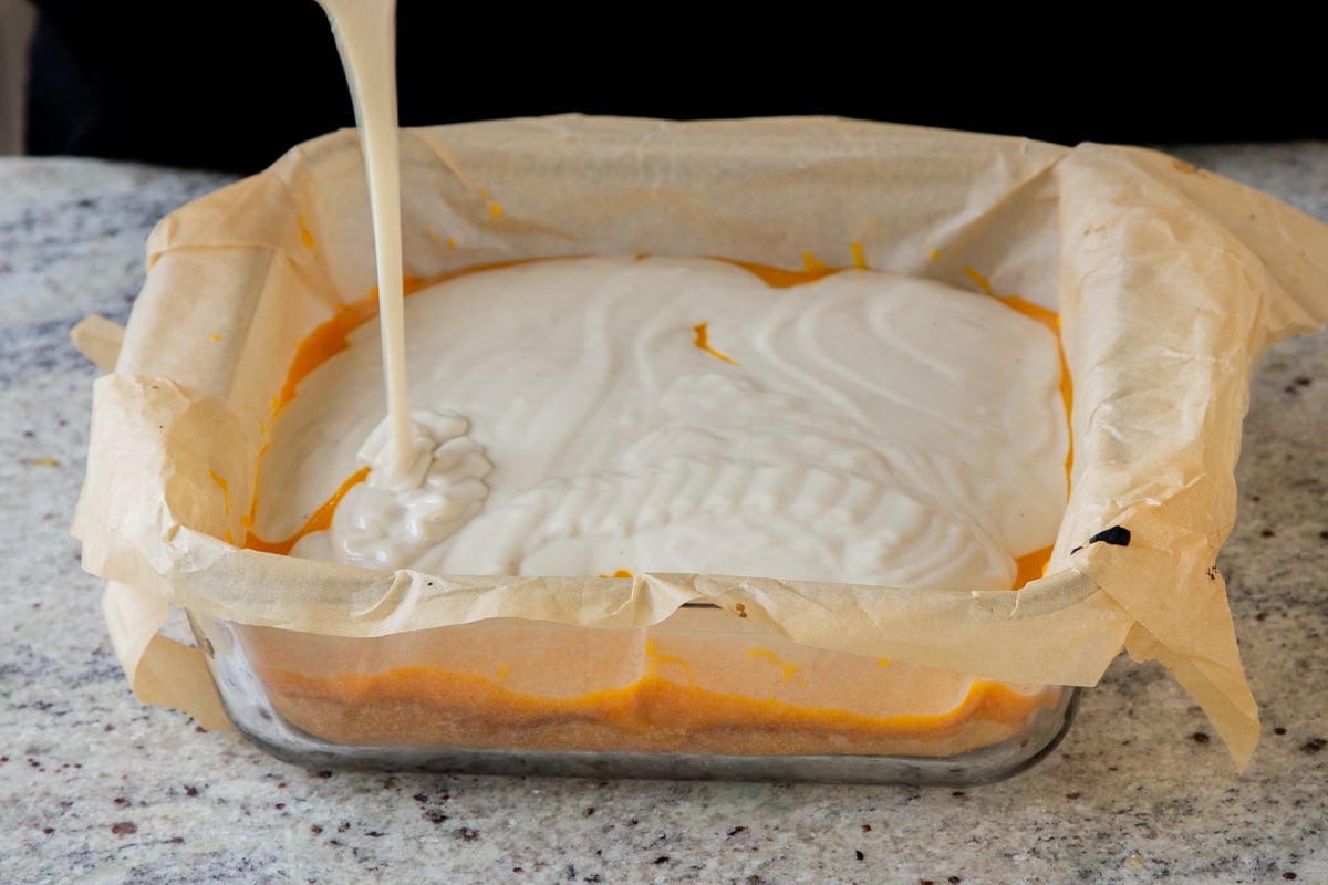 pouring cream mixture over the mango cake layer