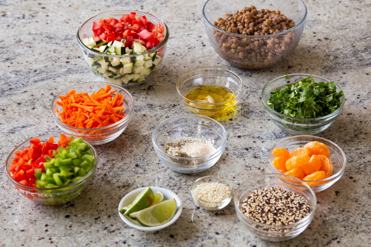 lentil, quinoa, and other salad and dressing ingredients in bowls on a kitchen counter