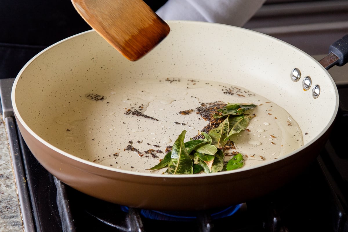 adding curry leaves to the pan of whole spices