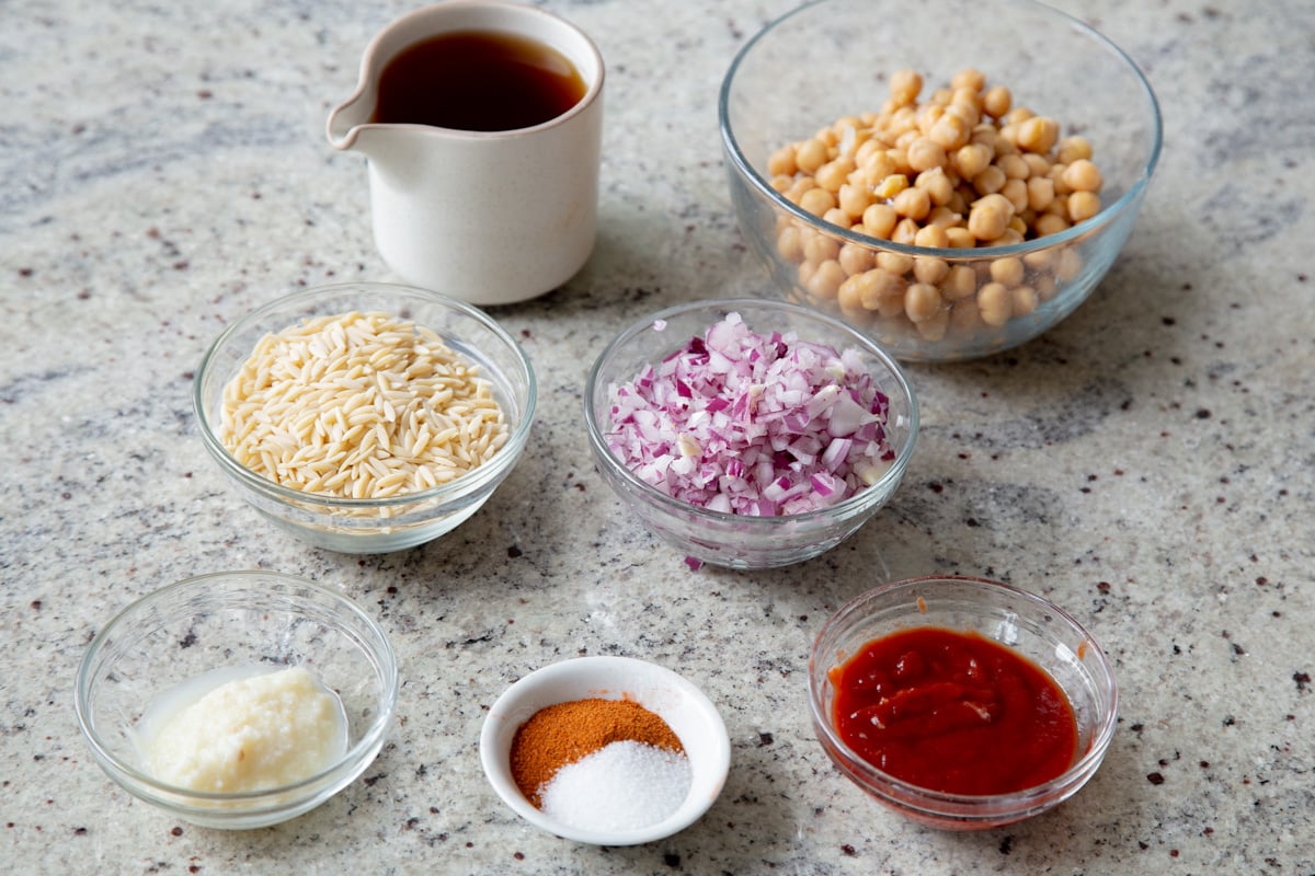 orzo, chickpeas, cajun spices, tomato paste, and garlic in cups on a kitchen counter