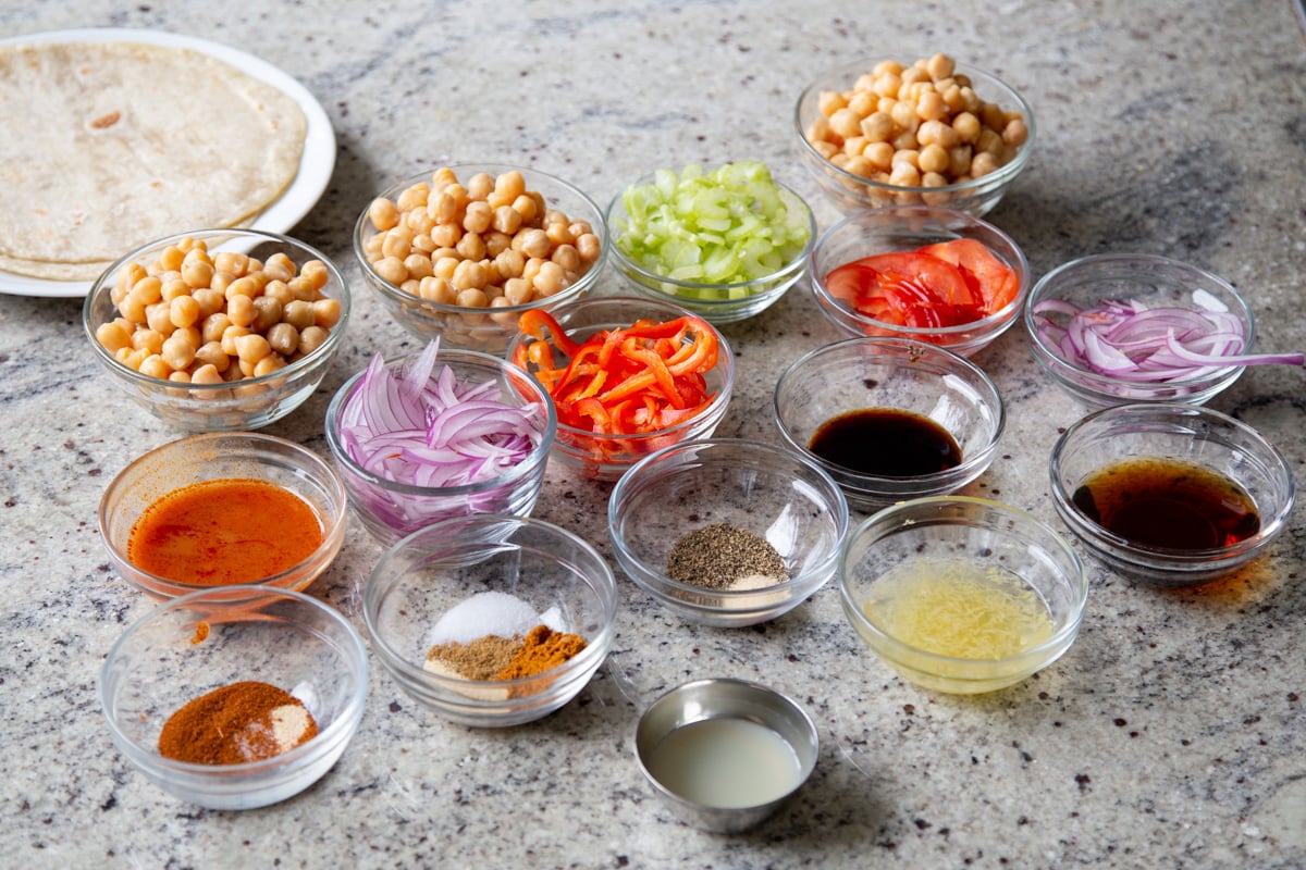 chickpeas, veggies, and other wrap ingredients in bowls on a kitchen counter