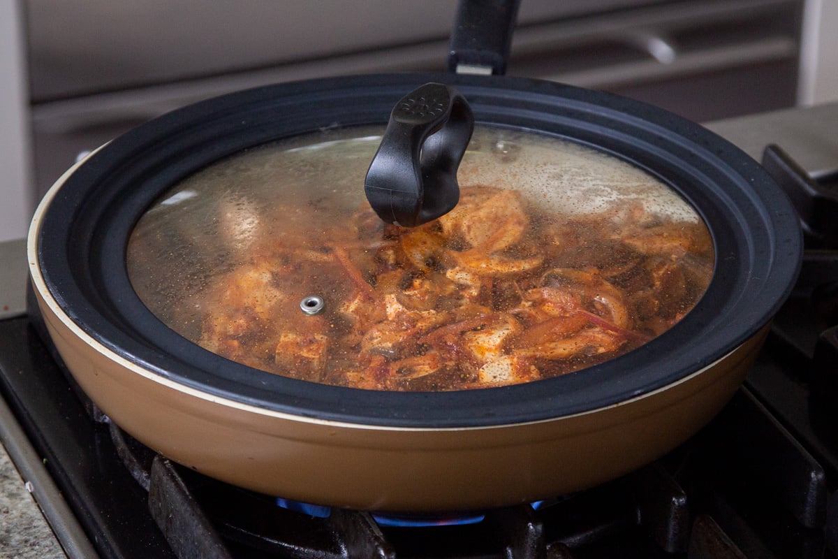 tofu and mushrooms cooking in the pan with the lid on