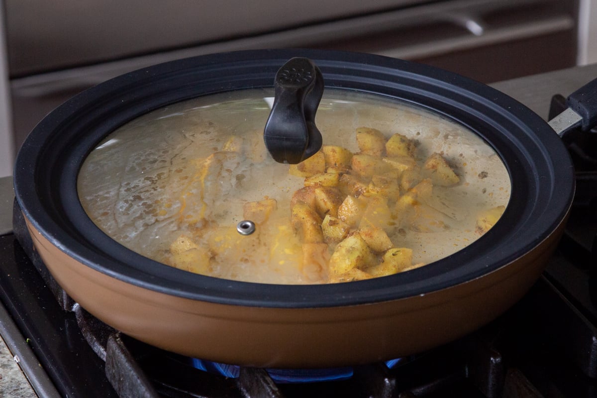 potatoes and spices cooking in the pan with the lid on