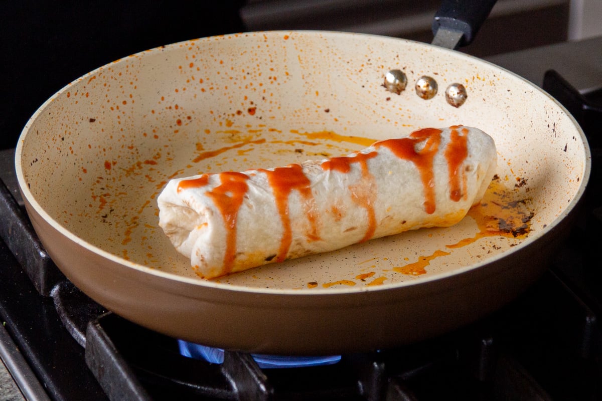 sealing the crispy tofu burrito with hot sauce in a pan