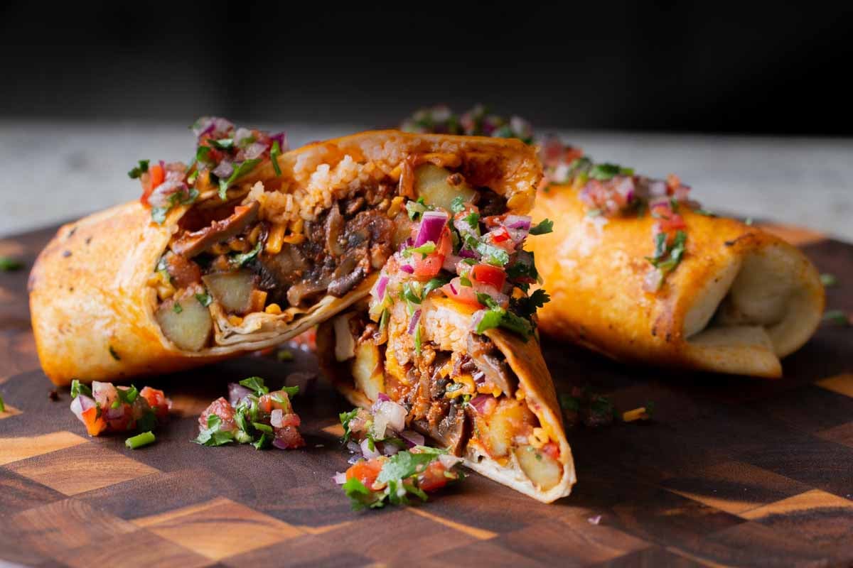 crispy tofu burrito on a wooden cutting board, cut in half so you can see the filling