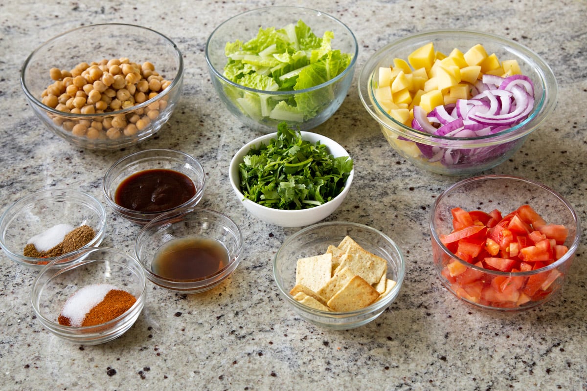 chickpeas, potatoes, onions, BBQ sauce, and other salad ingredients in bowls on a kitchen counter