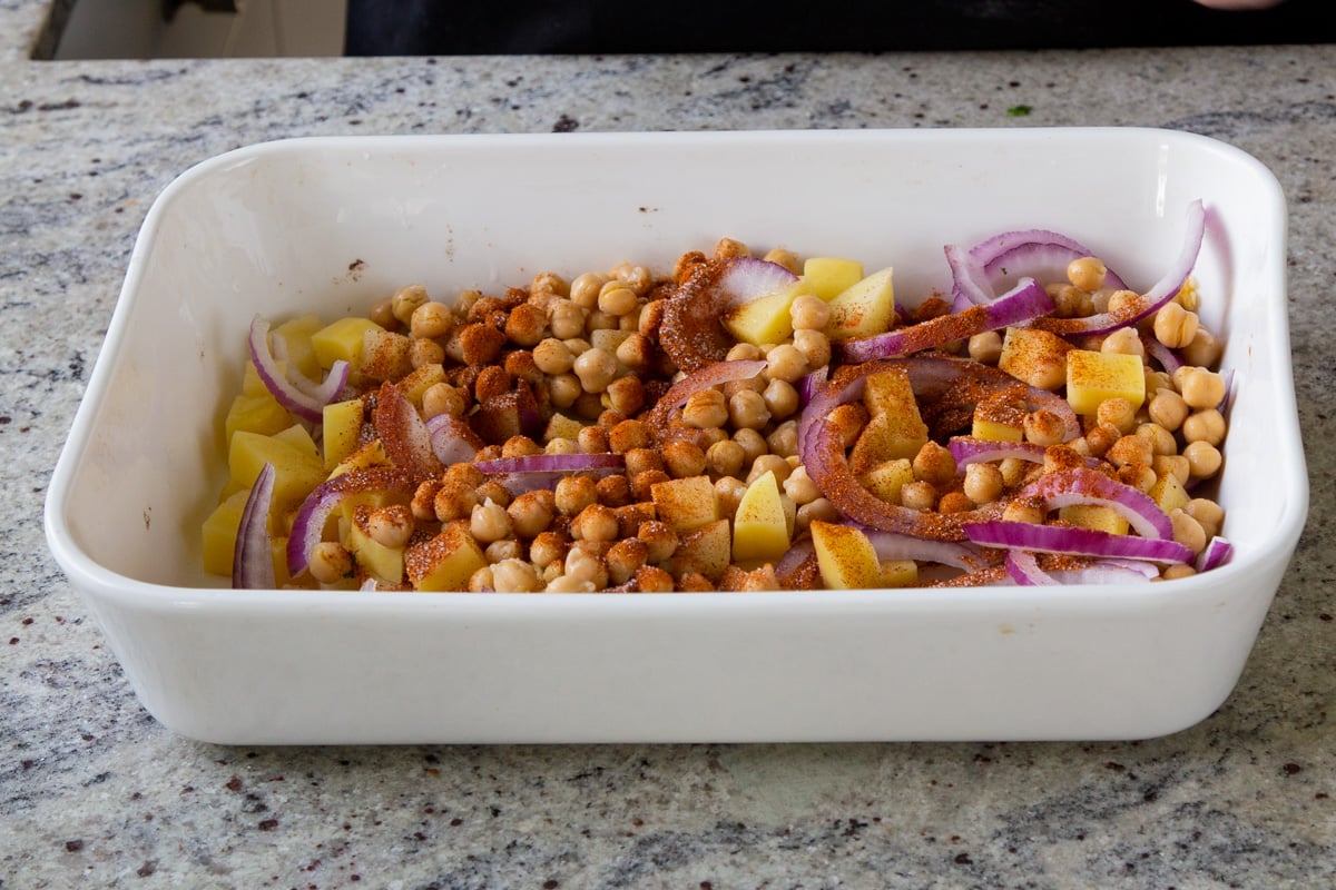 adding spices to chickpeas, onions, and potatoes