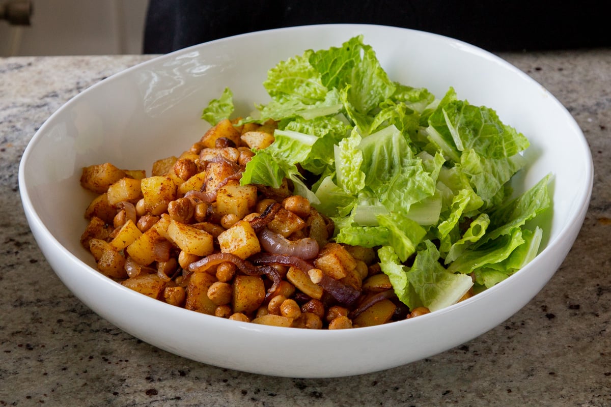 adding lettuce to the bowl of BBQ chickpeas and potatoes