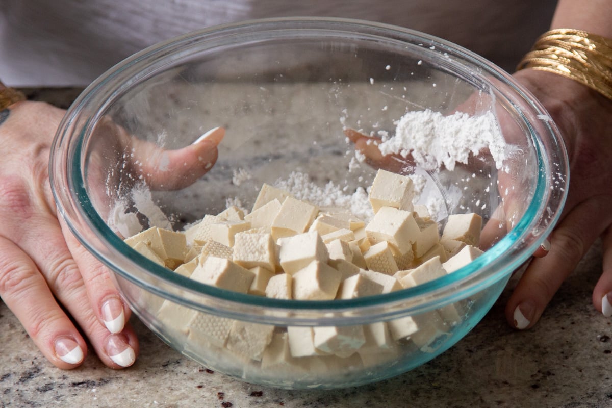 adding cornstarch to a bowl of cubed tofu